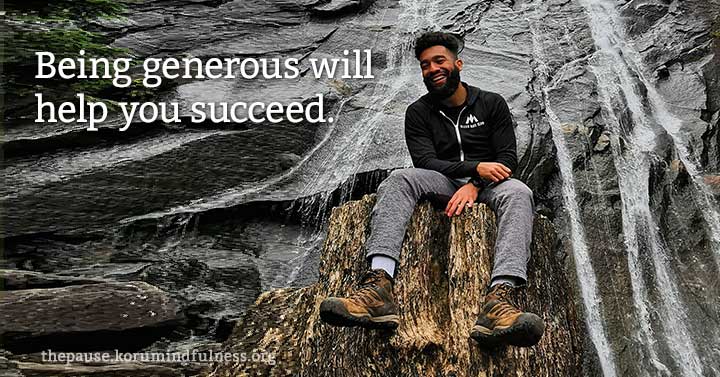 Photo of a man smiling and looking accomplished and sitting on a ledge on a waterfall